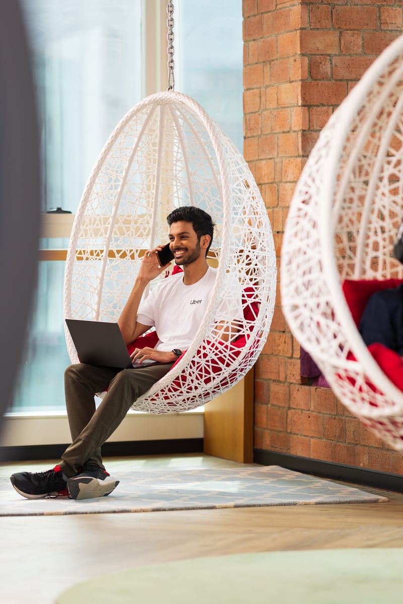 a person sitting in a chair with a laptop and a person on his phone