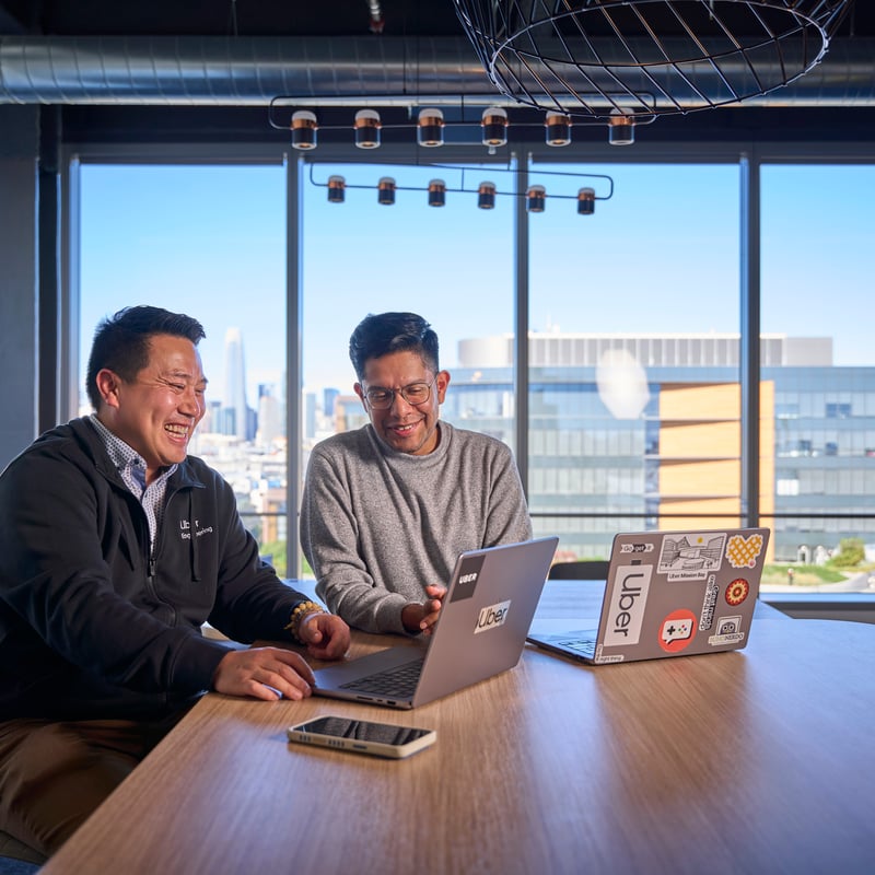 two men sitting at a table looking at a laptop